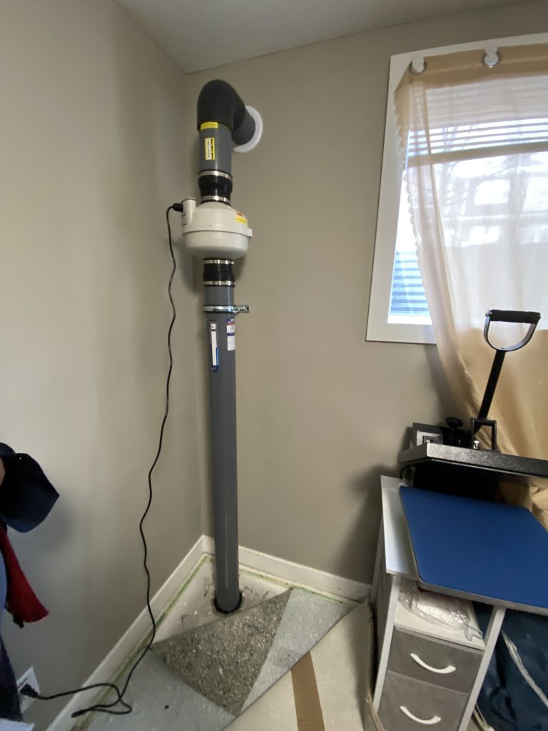 Sub-slab depressurization radon pipe running through finished basement wall in Airdrie home