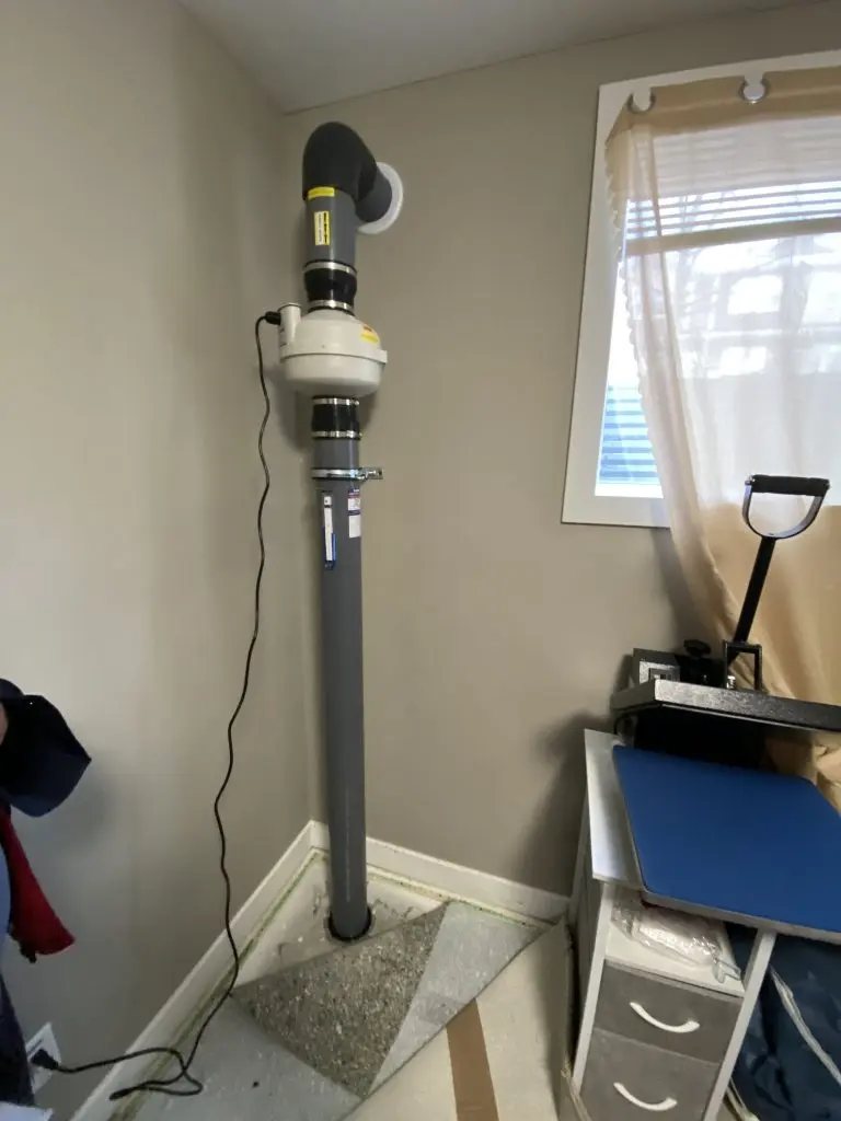 Sub-slab depressurization radon pipe running through finished basement wall in Airdrie home