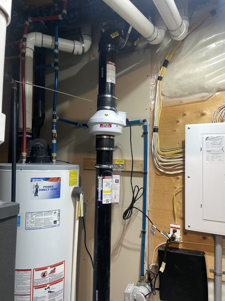 Radon fan motor installed in Airdrie basement utility room alongside water heater – Bye Radon mitigation system
