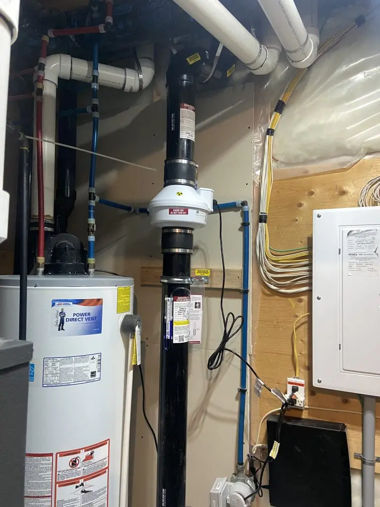 Radon fan motor installed in Airdrie basement utility room alongside water heater – Bye Radon mitigation system