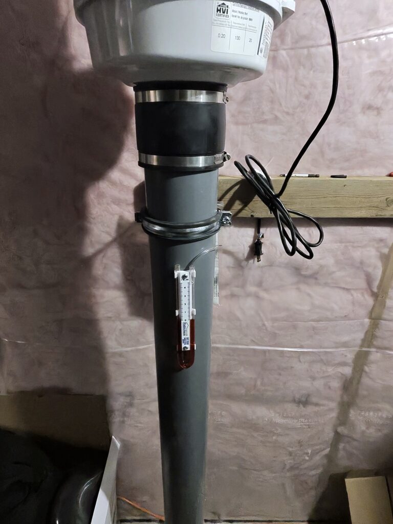 Close-up of radon mitigation fan with manometer pressure gauge confirming active system suction – Bye Radon Airdrie installation