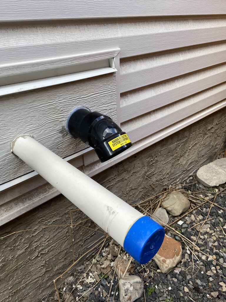 Radon mitigation system exhaust outlet on Airdrie home exterior — sub-slab depressurization pipe exit point installed by Bye Radon